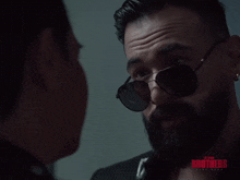 a man wearing sunglasses talks to another man with the words blood brothers on the bottom right