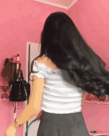 a woman with long black hair is standing in front of a pink wall in a room .