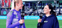 two women holding microphones on a soccer field with ads for invisalign and dazn in the background
