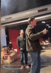 a man in a green jacket is standing in a room with boxes on the floor