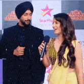 a man in a turban is talking into a microphone next to a woman in a yellow dress