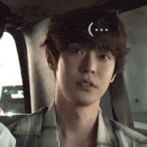 a young man is sitting in the back seat of a car with a smiley face on his head .