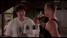 a man standing next to another man holding a scale that says ' muscle ' on it