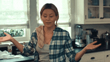 a woman wearing a plaid shirt is standing in a kitchen with her arms outstretched