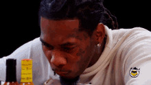 a man with a tattoo on his face looks at a hot sauce bottle