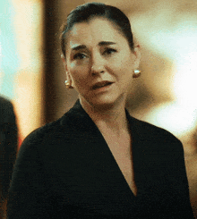 a woman wearing a black jacket and gold earrings looks sad