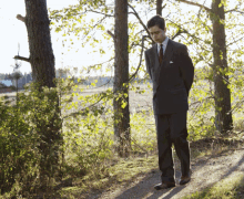 a man in a suit and tie is standing on a dirt path
