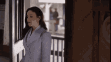 a woman in a blue suit is standing in front of a door with a wanted poster on the wall behind her
