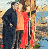 a group of people are standing next to a tree and one of them is wearing a red cape that says rise on it