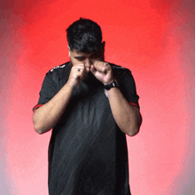 a man wearing a black shirt with a red stripe covering his face with his hands