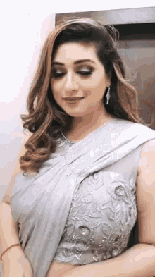 a woman in a gray saree is standing in front of a door and smiling .