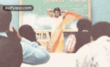 a woman in a saree is standing in front of a classroom full of people .