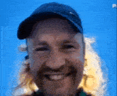 a man with long hair and a beard is smiling and wearing a blue hat .