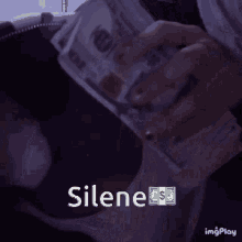 a person is holding a pile of money and the word silene is visible