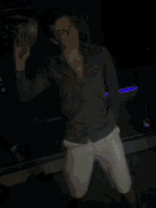 a man in a gray shirt and white shorts is dancing in the dark