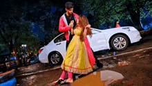 a man and a woman are dancing in a puddle in front of a white car .