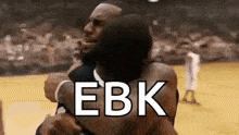 a couple of men hugging each other on a basketball court with the words ebk written on the bottom .