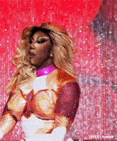 a drag queen is dancing on a stage in front of a red background .