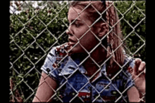 a woman is behind a chain link fence and looking through it