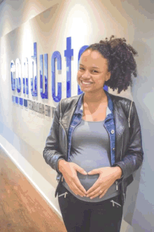 a pregnant woman holds her belly in front of a wall that says conduct