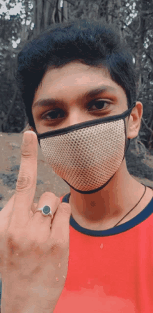 a young man wearing a face mask and a ring shows his middle finger