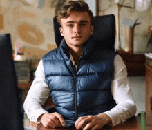 a man in a blue vest is sitting at a desk