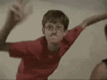 a young boy in a red shirt is making a peace sign with his hands .