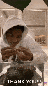 a man in a white hoodie is sitting at a table with a cake and says thank you !