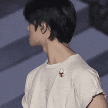 a man wearing ear buds and a white t-shirt has a pin on his shoulder