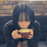 a woman drinking a cup of green tea with a brick wall in the background