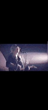 a man is playing a guitar and singing into a microphone while another man looks on .