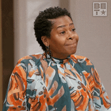 a woman in a colorful shirt is smiling in front of a sign that says be t