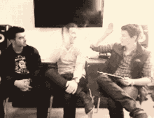 a man wearing a t-shirt that says ' nirvana ' on it sits with two other men