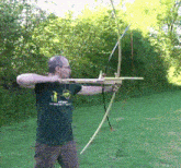 a man in a green shirt that says archery is holding a bow and arrow