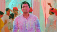 a man in a white shirt is standing in front of a group of people covered in colored powder .