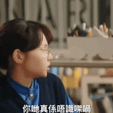 a woman wearing glasses and a blue shirt has chinese writing on her chest