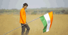 a man in an orange shirt is carrying a flag in a field