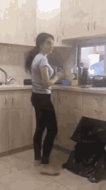 a woman is standing in a kitchen in front of a sink and a window