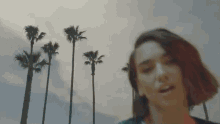 a woman stands in front of palm trees and a cloudy sky
