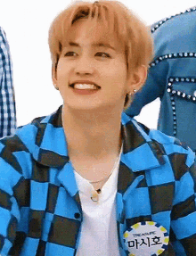 a young man wearing a blue and black checkered shirt and a white t-shirt is smiling .