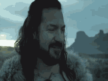 a man with long hair and a beard wearing a fur coat is standing in a field .