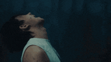 a man in a white tank top is looking up in the dark