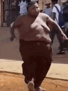 a very fat man without a shirt is running down the street .