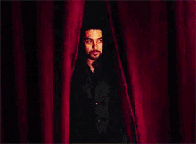 a man standing behind a red curtain looking at the camera