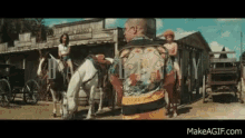 a man in a hawaiian shirt is standing in front of a horse drawn carriage in a western town .