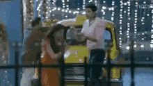 a man is standing next to a woman in front of a yellow taxi cab .