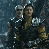 a man with a tattoo on his face is standing next to another man in armor