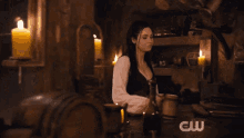 a woman sits at a table with candles and a cw logo in the background