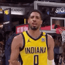 a basketball player wearing a yellow jersey with the number 0 on it is standing in front of a basketball net .