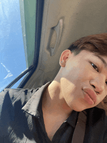 a young man taking a selfie in a car with a blue sky behind him